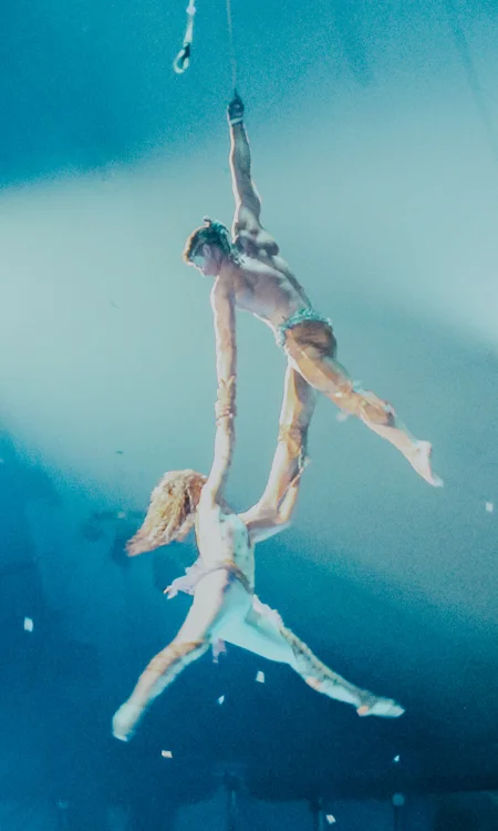 Aerial performers suspended above stage during live entertainment show with dramatic lighting and immersive atmosphere