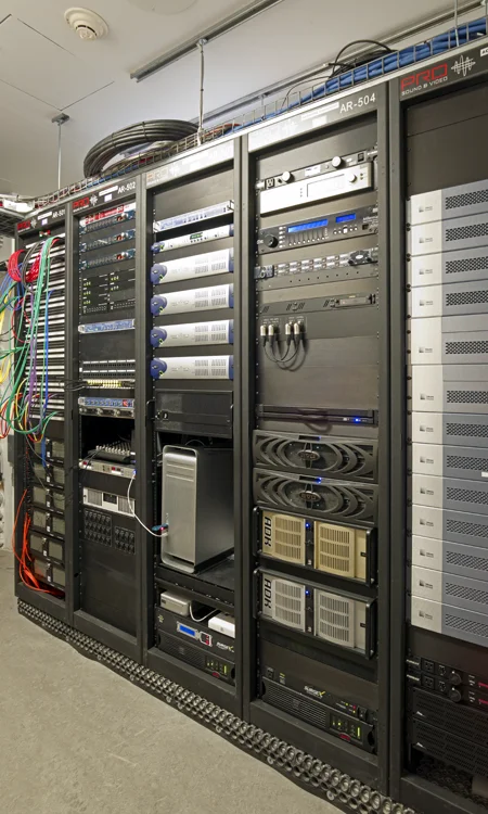 Professional AV equipment racks with audio processing, network distribution, signal routing, and system control hardware supporting a performing arts venue.