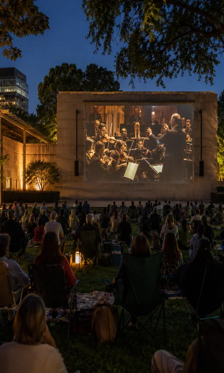 Audience at an outdoor evening performance in SoundScape Park watching a large projected concert image