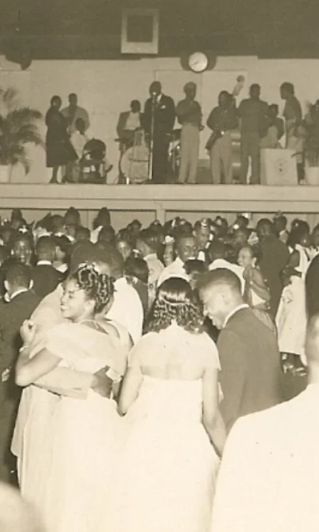 Historic black-and-white photo of guests dancing at Sunset Lounge with a live band performing above the crowd
