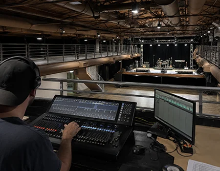 Technician operating a lighting control console from the control booth overlooking the stage at Sunset Lounge