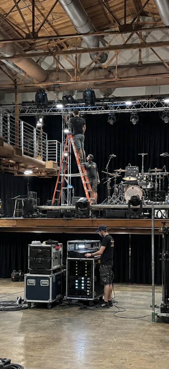 Technicians setting up stage rigging, lighting, and audio equipment inside an empty Sunset Lounge venue before a concert