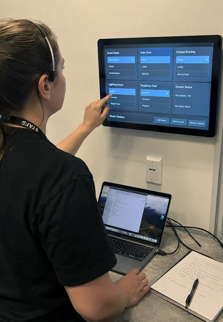 Venue operator using a wall-mounted touchscreen control system in a technical booth overlooking a live event space