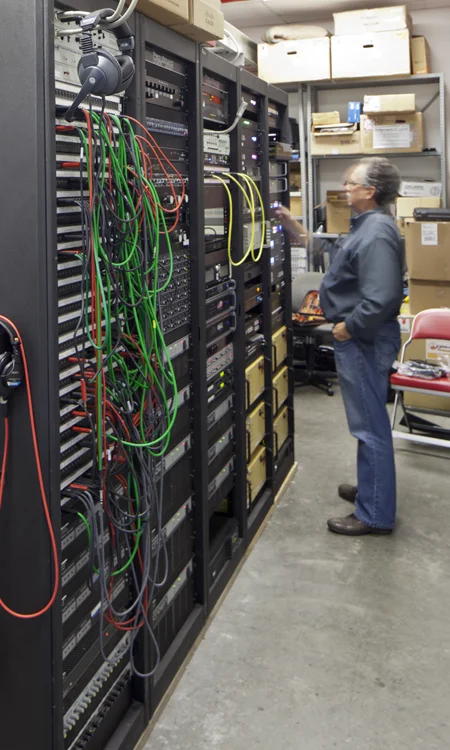 Technician working beside audio equipment racks and cabling for the Ohio Stadium sound system expansion.